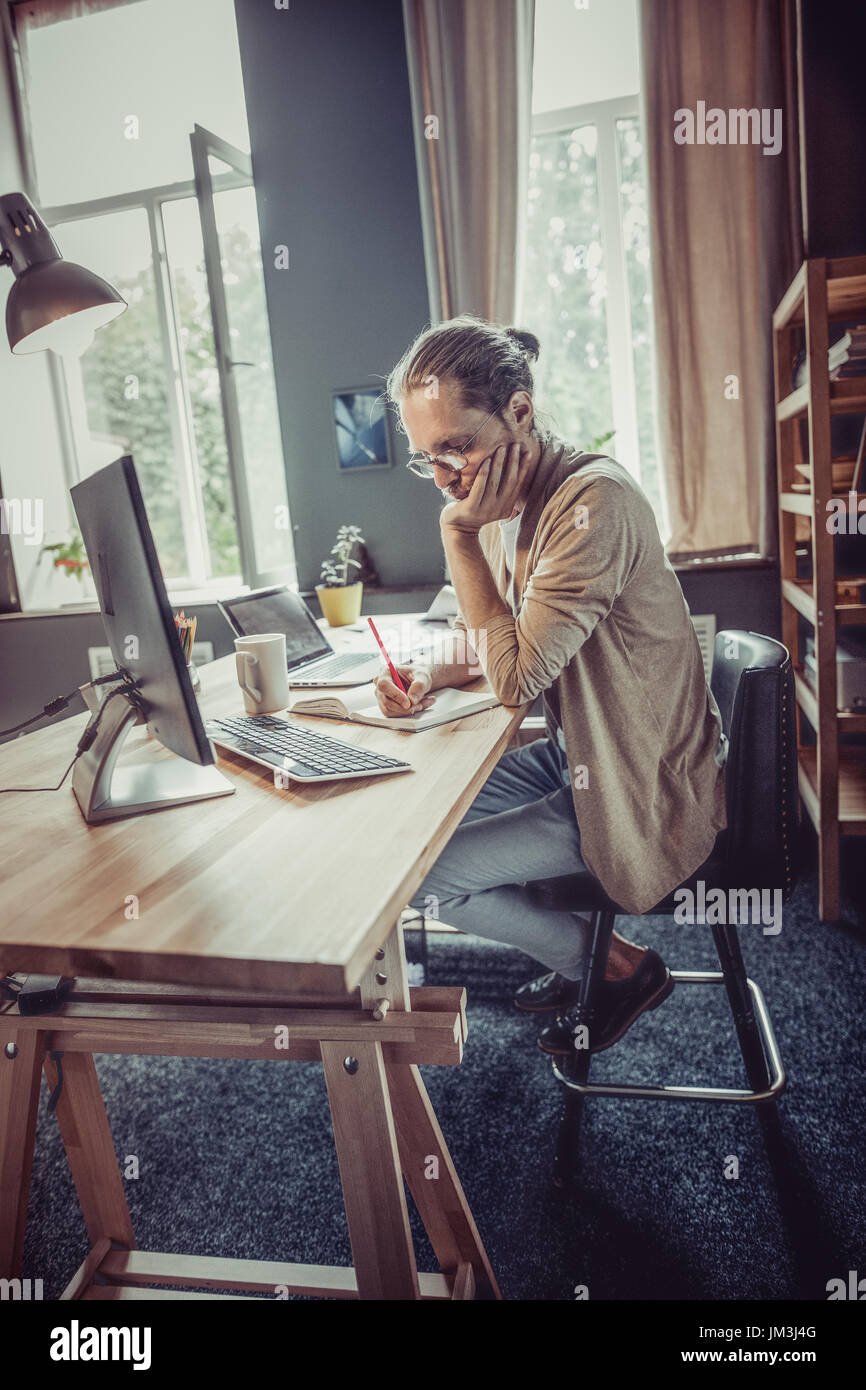 Seitliche Sicht auf Mann arbeitet auf Freelance bei Holztisch. Freelancer bei Arbeitsprozess, Notizen auf Papier. Stockfoto