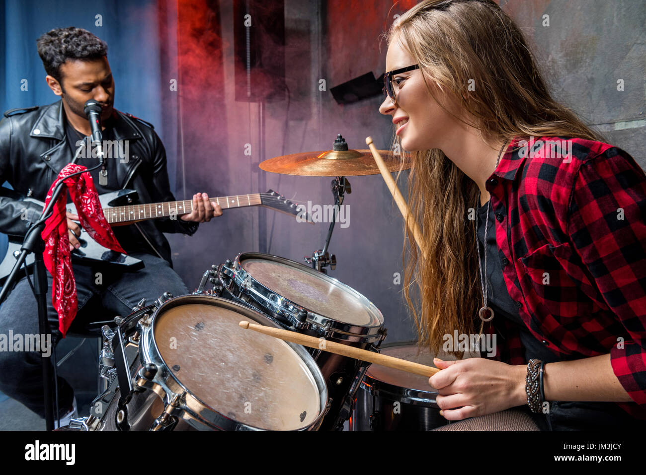 Seitenansicht der Frau spielt Schlagzeug mit Mann spielt Gitarre, Rock Band-Konzept Stockfoto