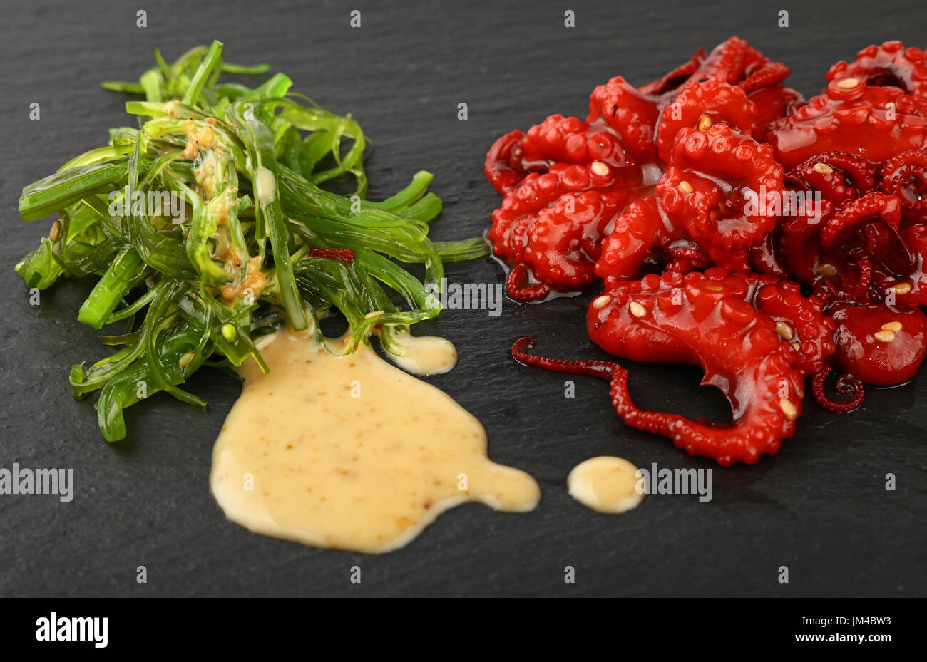 Meeresfrüchte, die kleinen ganz rot Baby-Oktopus-Salat mit grünen Algen und Erdnuss-sauce auf Schiefer Tafel, Nahaufnahme, hoher Winkel Stockfoto