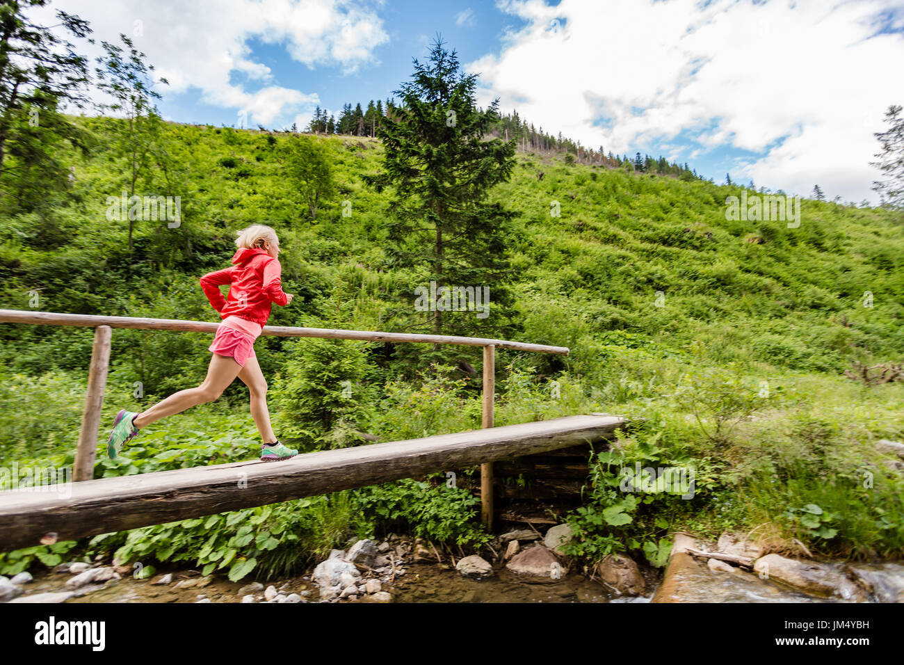 Junge Frau läuft in Bergen an sonnigen Sommertag. Weibliche Trailläufer Brücke auf einem Bergfluss. Sport und Fitness-Konzept im Freien in n Stockfoto