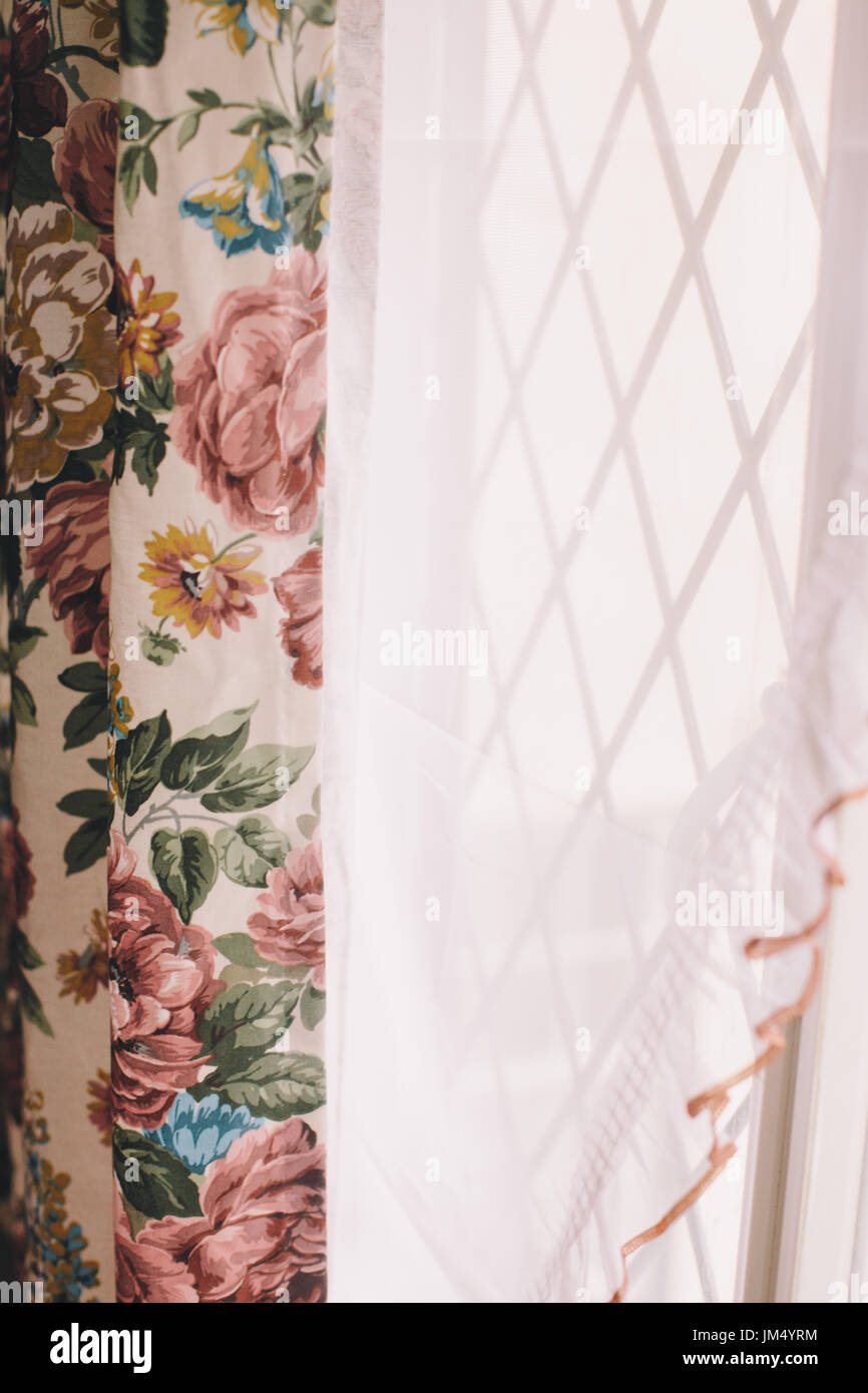 Vintage Vorhänge mit Blumenmuster und einem weißen Vorhang vor einem Bleihaltigen Licht Fenster Stockfotografie