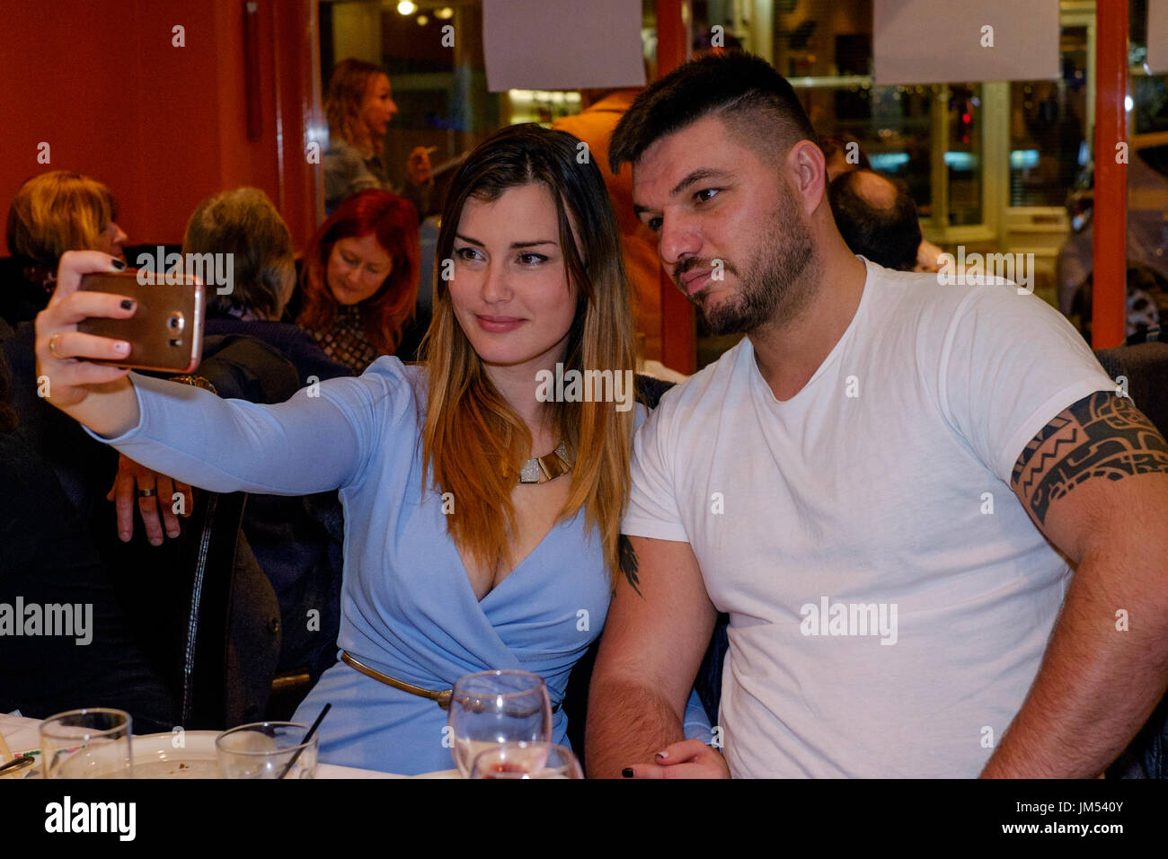 Junge hübsche Frau mit einem Smartphone eine selfy sich und Ihre männlichen Partner in einem Restaurant zu nehmen Stockfoto