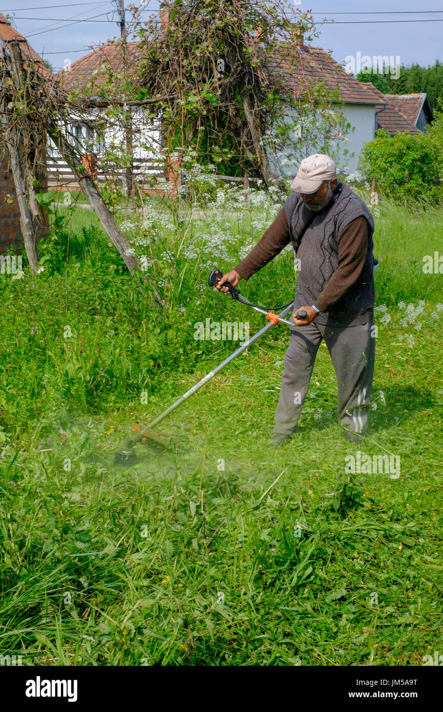 Mann mit einem Trimmgerät zu lang geschnitten grass im Garten eines ländlichen Hauses in einem Dorf in Ungarn Zala Grafschaft Stockfoto