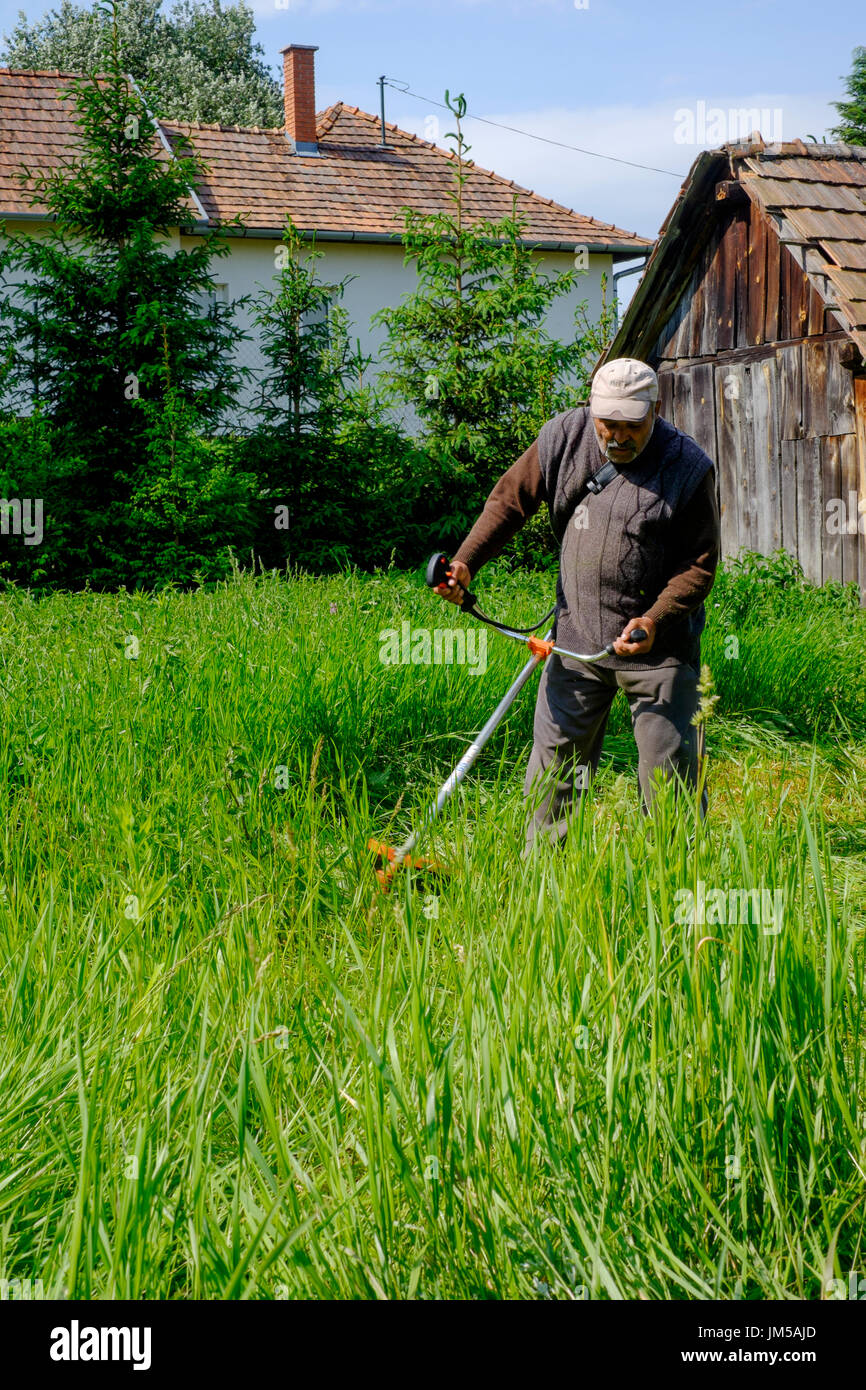 Mann mit einem Trimmgerät zu lang geschnitten grass im Garten eines ländlichen Hauses in einem Dorf in Ungarn Zala Grafschaft Stockfoto