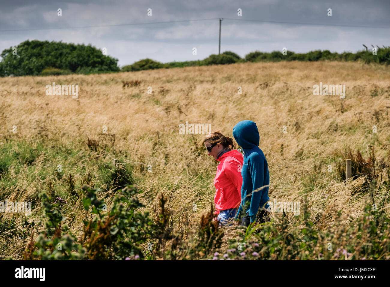 Zwei junge Frauen in Hoodies Wandern in Felder an Bempton Klippen RSPB Reserve, UK. Eine Frau hat ihre Kapuze, Kapuzenjacke Hoodie. Stockfoto