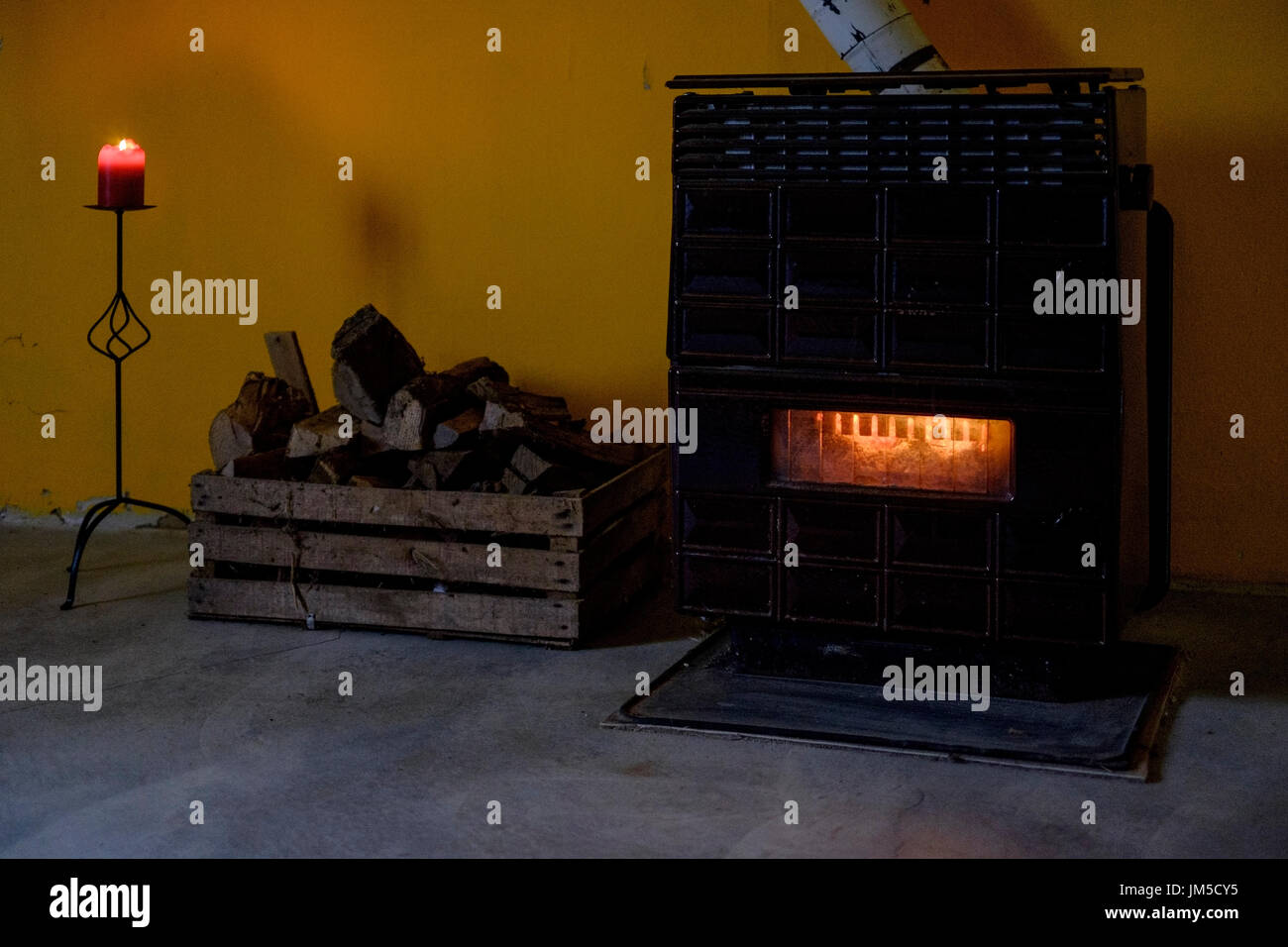 Glühende Holzofen und brennende Kerze in einem verdunkelten Raum Stockfoto