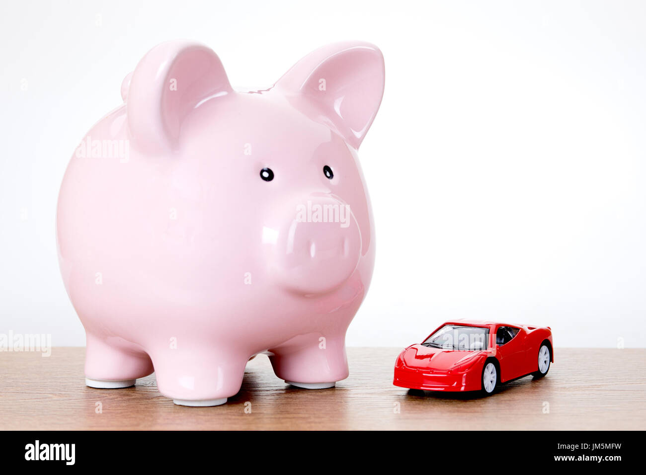 Sparschwein mit einem bunten roten Spielzeug Modellauto auf einem Holztisch in eine Idee des Sparens für Eigentum, Träume und Sehnsüchte oder Kosten für die Instandhaltung einer Stockfoto