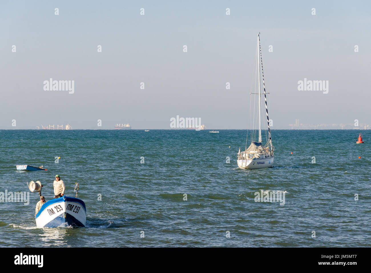 Fischer in kleinen Boot nähert sich der Küste mit paar große Schiffe im Hintergrund, Pomorie, Bulgarien Stockfoto