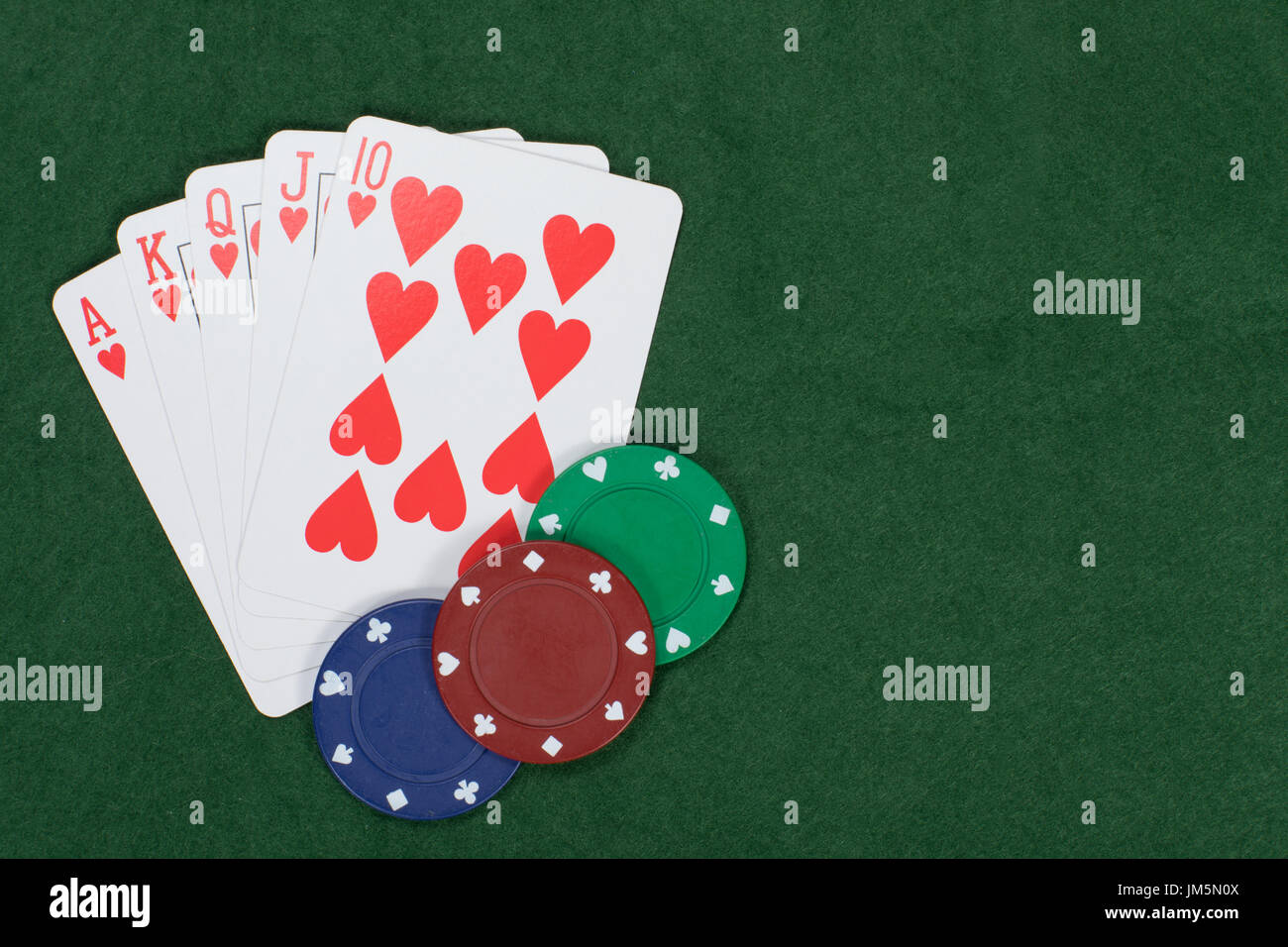 Poker und Glücksspiel Gewinnerhand mit Casino-Chips mit einem geraden Royal Flush in Herzen angezeigt auf einem grünen Filz-Hintergrund mit Textfreiraum Stockfoto
