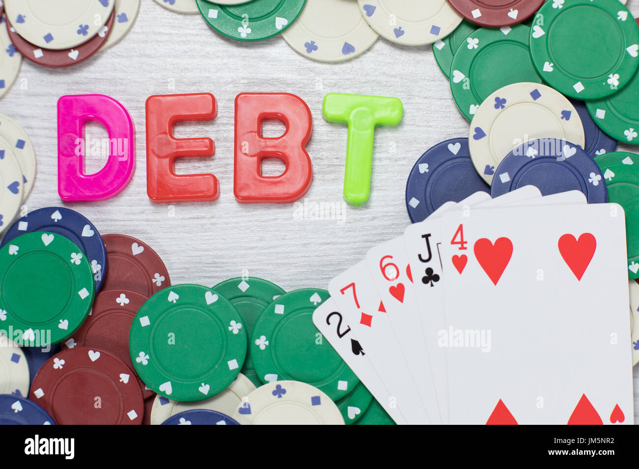 Spielschulden nach einer Pechsträhne in einem konzeptionellen Bild mit einer schlechten Hand Poker Karten aufgefächert auf Casino-Chips mit dem Wort - Schulden - col Stockfoto