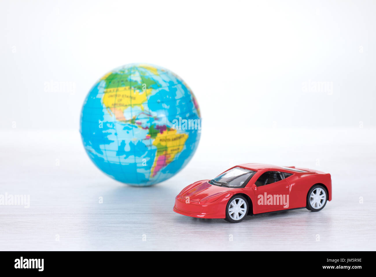 Sportlich rot Spielzeugauto mit einer Weltkugel in ein Konzept der weltweiten Reiseziele oder Speichern des Planeten durch den Einsatz von umweltfreundlichen Kraftstoffen o Stockfoto