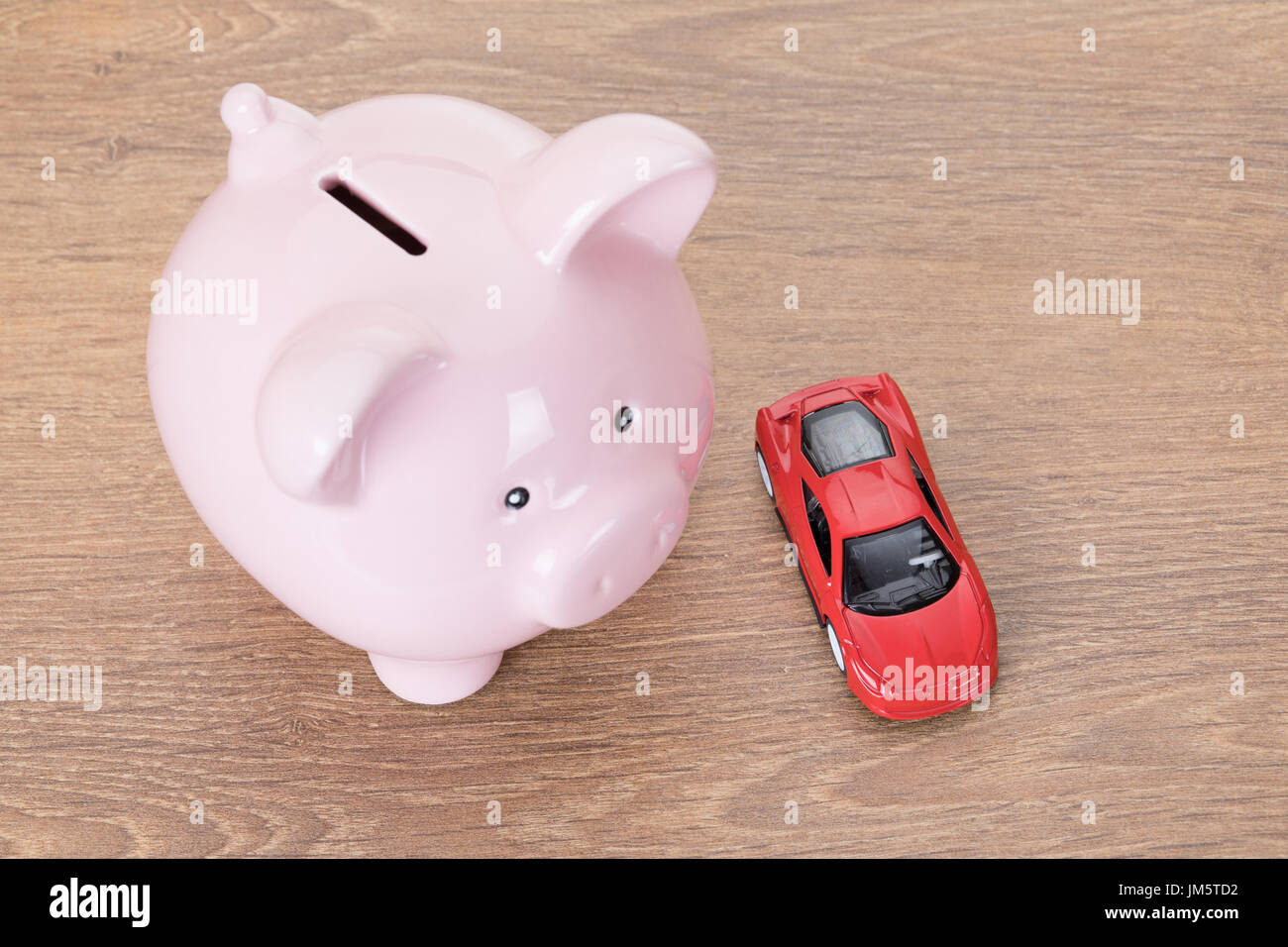 Rosa Sparschwein mit roten Spielzeugauto in einem Konzept von Besitz, Kauf, Kosten für den Betrieb der Fahrzeug- und Wartung auf Holz von oben gesehen Stockfoto