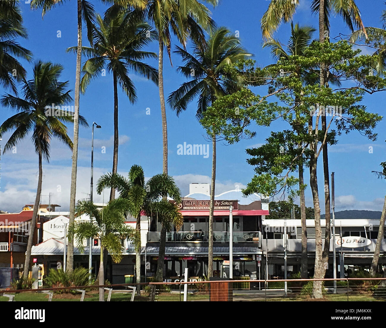 Cairns Esplanade Geschäftsviertel beginnt auf der gegenüberliegenden Straßenseite, vorbei an Palmen, wo Iyara durch Sakare Thai Restaurant prominent im Obergeschoss ist Stockfoto
