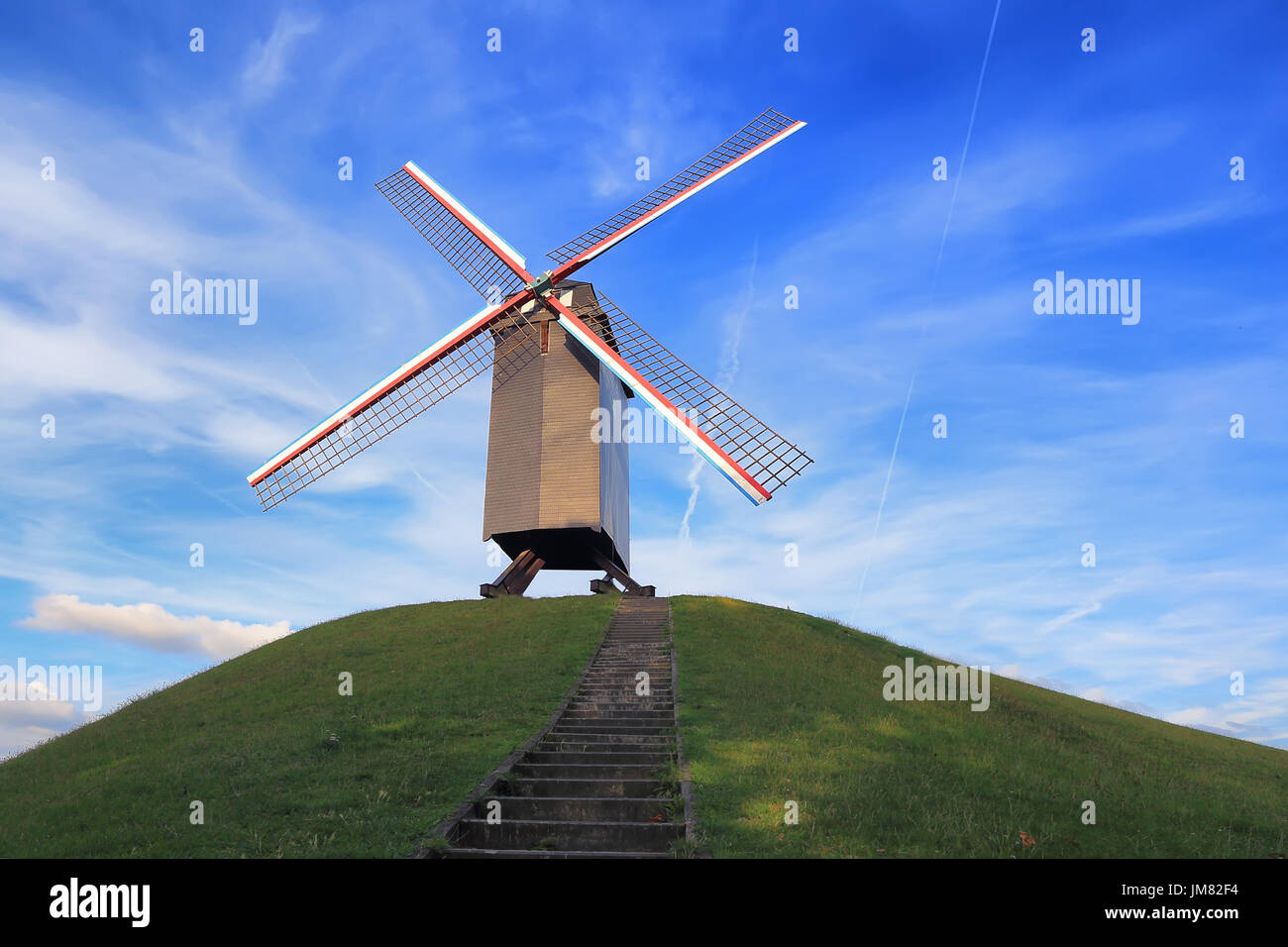 Windmühle auf grünem Hügel an einem sonnigen Tag. Retro-Windmühle auf blauen Himmelshintergrund. Wahrzeichen von Brügge. Stockfoto
