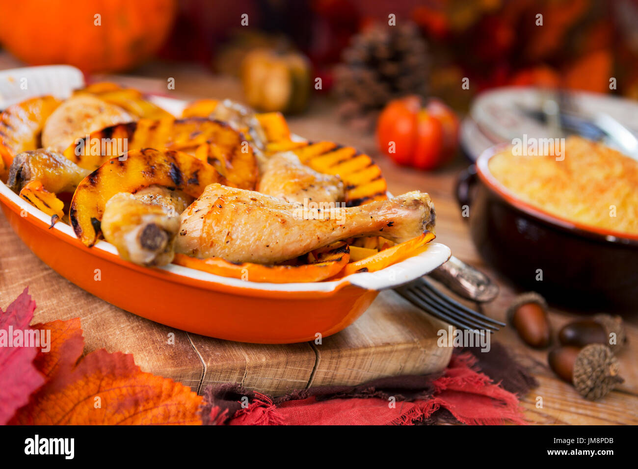 Eine Kasserolle mit Backofen gebratenes Huhn und gegrilltem Kürbis auf einem rustikalen Tisch mit herbstlichen Dekorationen. Stockfoto