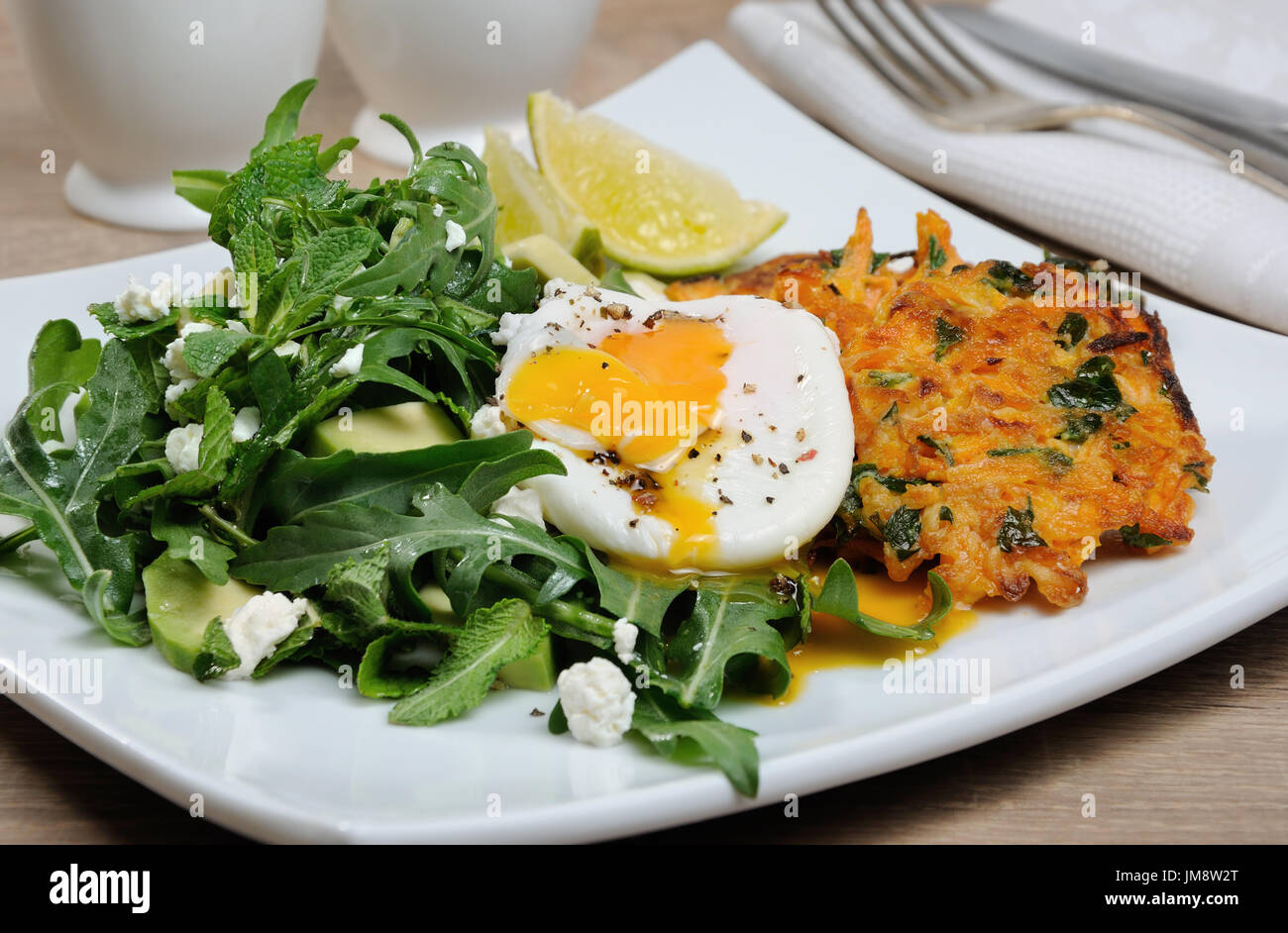 Brunch-Idee. Pochiertes Ei mit Kürbis-Spinat-Pfannkuchen und Garnitur aus Rucola, Avocado, Minze und ricotta Stockfoto