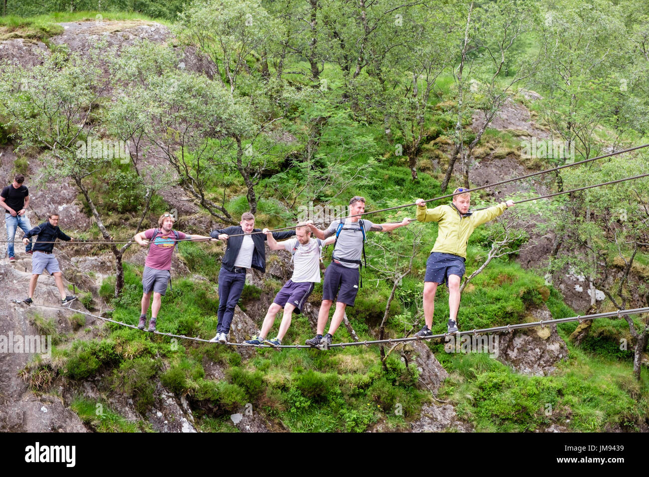 Sechs Männer schwingen auf Steall Drahtbrücke über Wasser von Nevis River Flickschusterei. Glen Nevis, Fort Willaim, Highland, Schottland, UK, Großbritannien Stockfoto