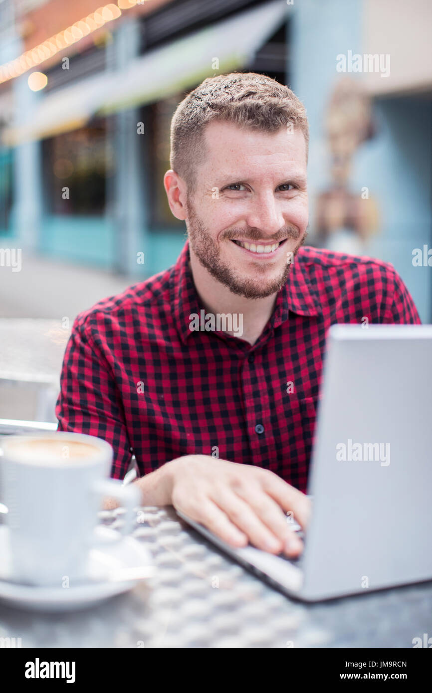 Porträt des jungen Mannes im Outdoor-Cafe auf Laptop Stockfoto