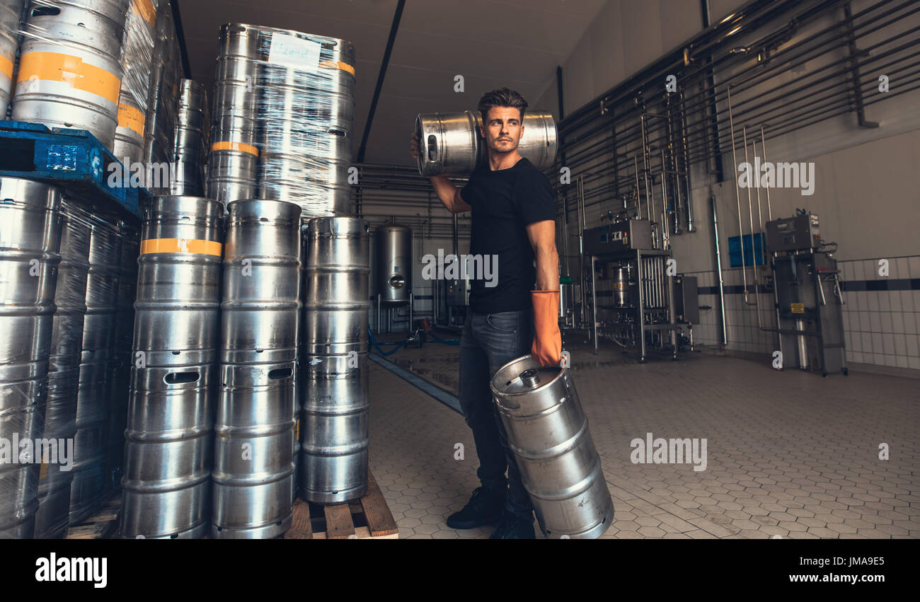 Junge männliche Brauer Keg werkseitig Brauerei tragen. Junger Mann mit Metall Bierfässer auf Lager. Stockfoto