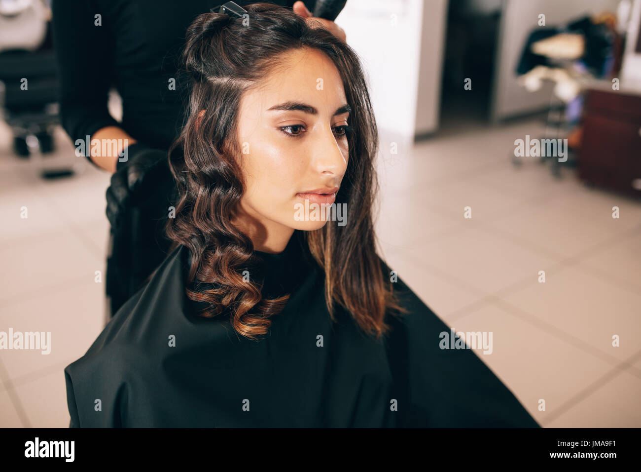 Nahaufnahme der jungen Frau auf dem Salon, ihre Haare gestylt. Friseur, glattes Haar in Locken verwandeln. Stockfoto