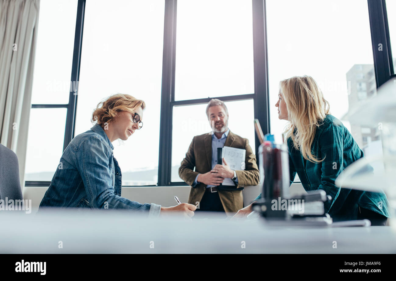 Geschäftsleute in modernen Büro. Geschäftsfrau sitzt an ihrem Schreibtisch mit Kollegen stehen. Stockfoto