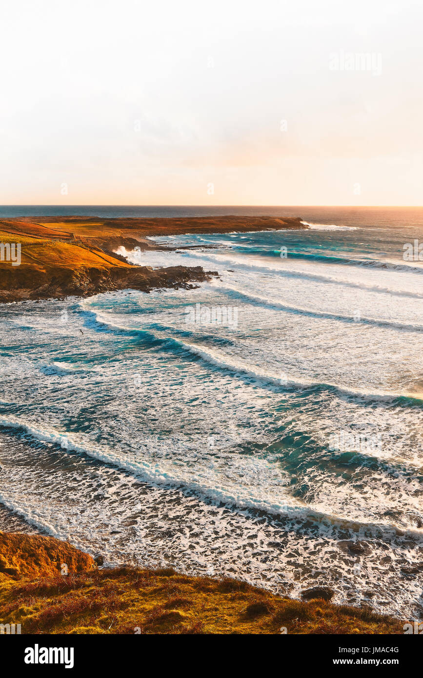 Irische Strand bei Sonnenuntergang im Sommer mit einem blauen Himmel und Wellen gegen die Felsen zertrümmern Stockfoto