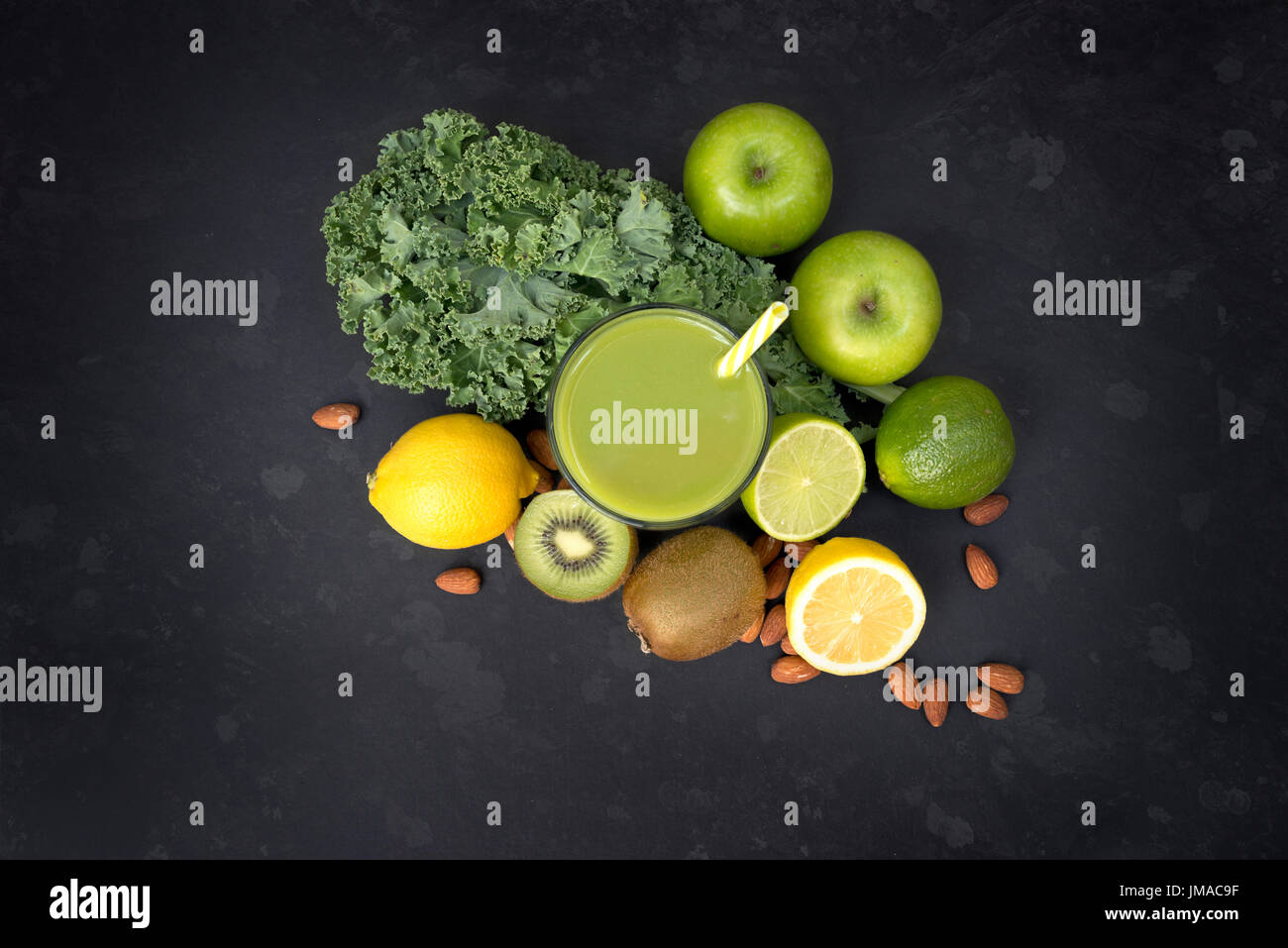 Gesundes Wohnen-Konzept mit einem Glas grüner Smoothie umgeben von Kohl, Äpfel, Mandeln, Limetten und andere Obst und Gemüse auf einem dunklen Hintergrund. Stockfoto