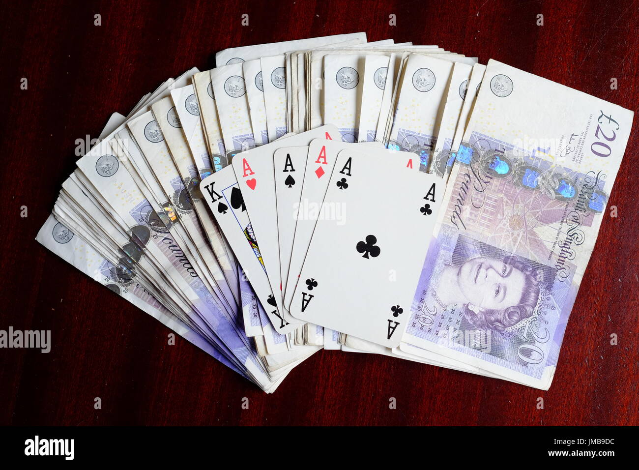 Vier Asse und ein König, eine glückliche gewinnende Pokerhand und ein Vermögen in 20 Pfund-Noten auf einem dunklen Tisch Stockfoto