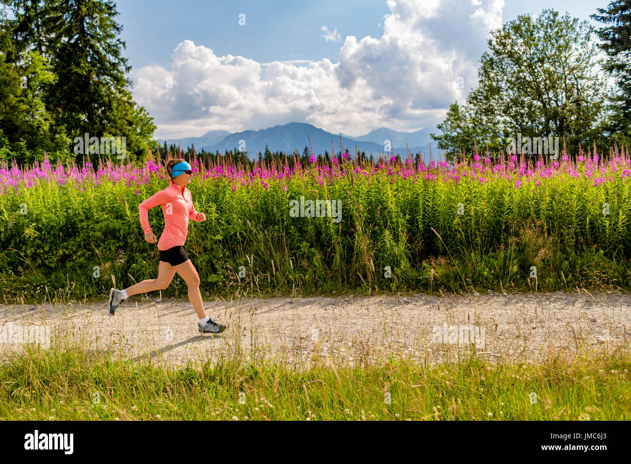Junge Frau läuft in Bergen an sonnigen Sommertag. Sportlerin Trailläufer auf Landstraße. Sport und Fitness-Konzept im Freien in der Natur. Stockfoto