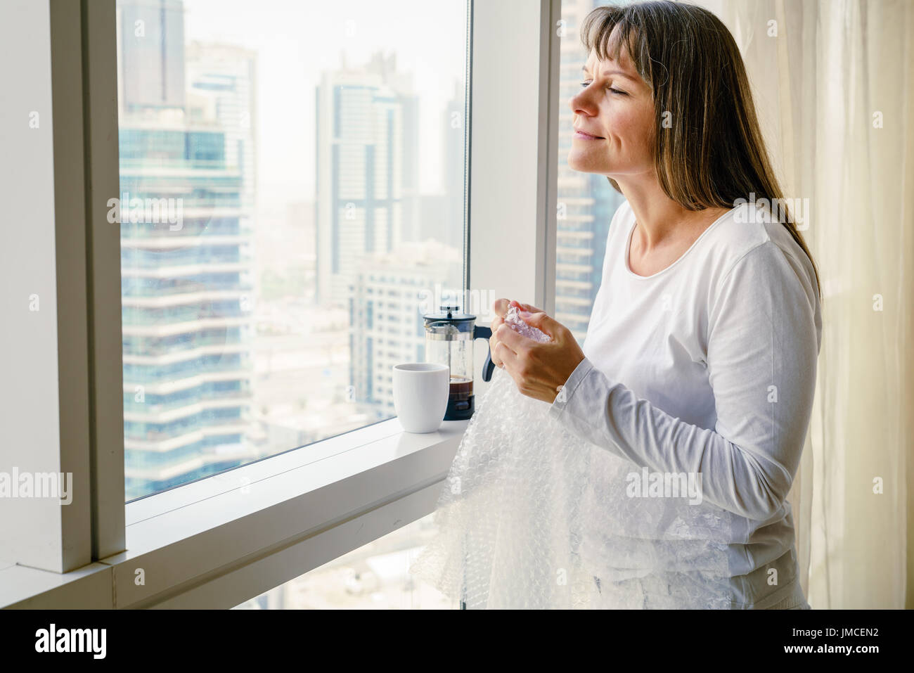 Reife Frau am Fenster ist Stress die Freigabe durch knallende Luftpolsterfolie Stockfoto