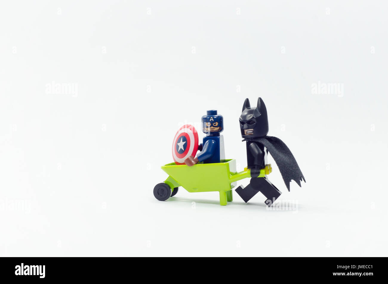 LEGO Kapitän Amerika Minifigur sitzen auf Schubkarre während Batman einschieben, isoliert auf weißem Hintergrund. Stockfoto