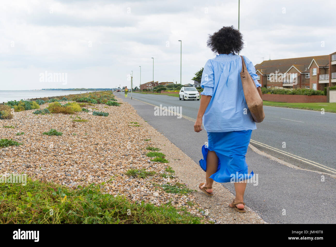 Frau zu Fuß entlang einer Straße direkt am Meer von einem Strand an einem windigen Tag. Stockfoto