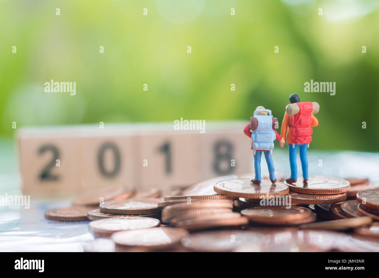 Miniatur Rucksacktouristen auf dem Stapel Münzen schlagen auf ihren Rücken zu und freut sich auf hölzerne Zahlen 2018, Reisen und Business-Konzept. Stockfoto