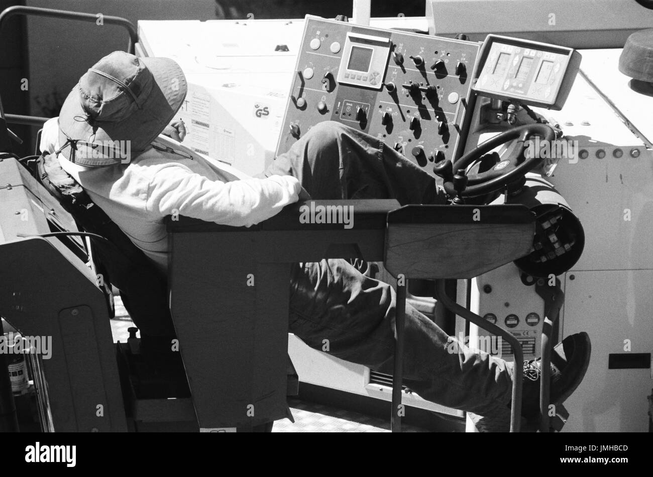 Ein Bauarbeiter für amerikanische Asphalt lounges auf seine Ausrüstung während des Wartens auf andere Mitarbeiter ihre Aufgaben während einer Straßenbau und resurfacing Projekt im Stadtteil San Francisco Bay Area von San Ramon, Kalifornien, 26. Juni 2017 abgeschlossen. Stockfoto