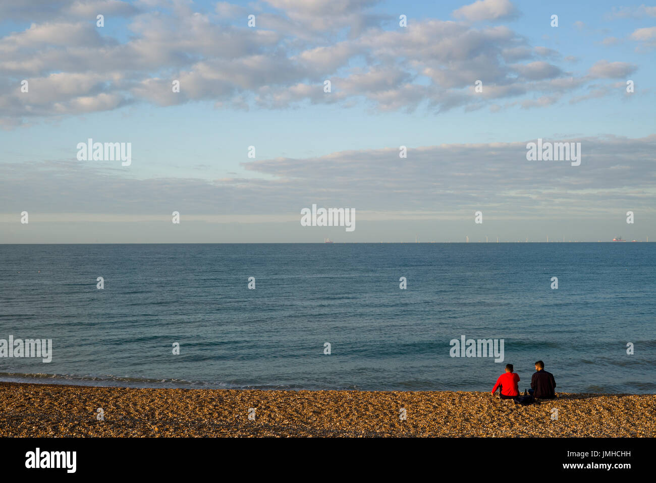 Zwei Männer sitzen auf leeren Strand, Hove, Sussex Stockfoto