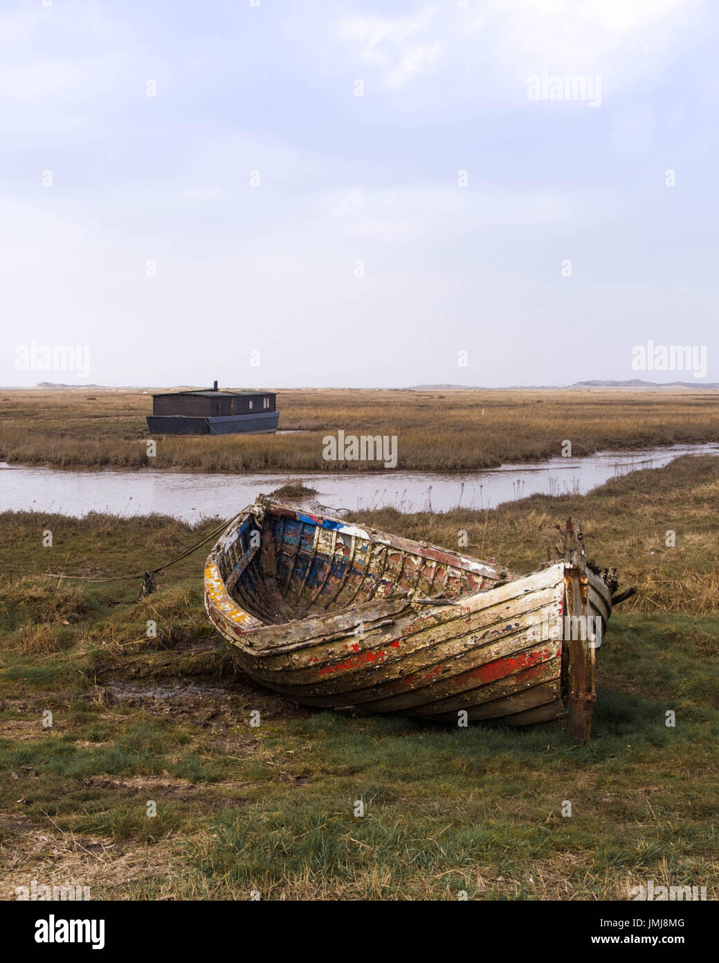 Abblätternde Farbe auf einem verwitterten Ruderboot mit Hausboot geerdet bei Ebbe im Hintergrund Stockfoto