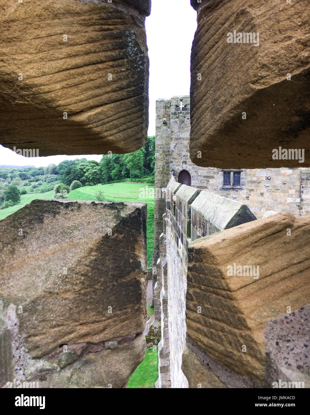 Ein Bogenschütze Blick durch den Pfeil Schlitz entlang der steinernen Zinnen einer normannischen Burg in England. Stockfoto