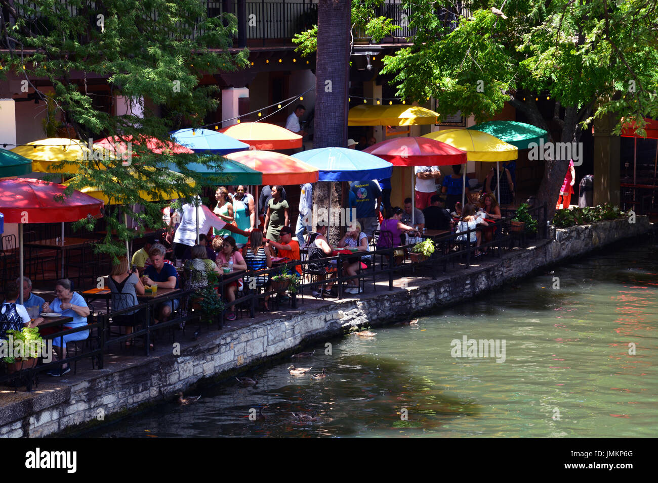 Leute sitzen an den Sonnenschirm beschattet Restaurant Tischen entlang des San Antonio Riverwalk. Stockfoto