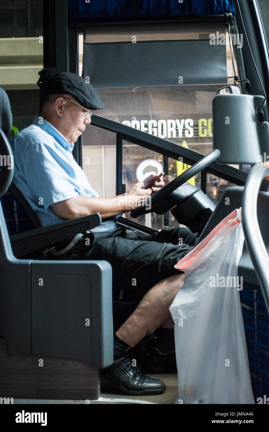 Ältere asiatische Busfahrer suchen auf seinem Handy während der Einnahme einer Pause auf der Straße von New York City Stockfoto