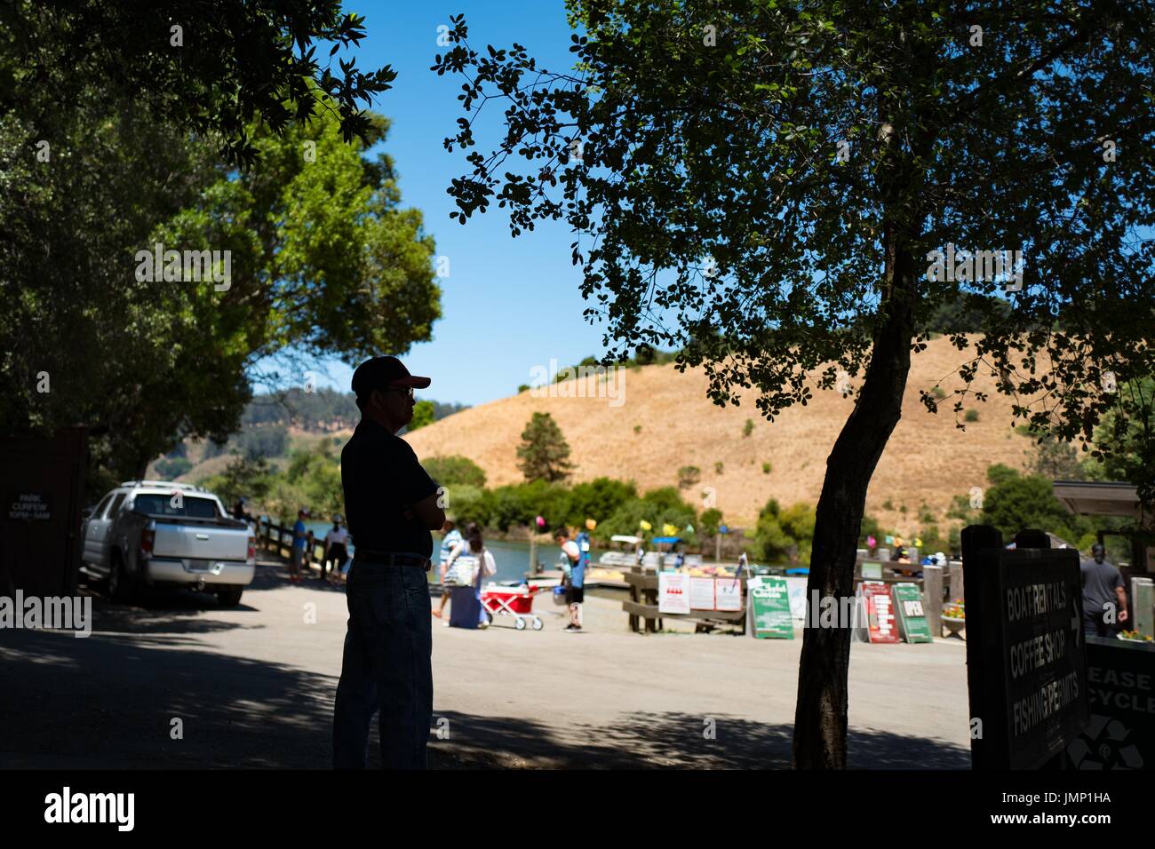 Die Silhouette eines Mannes, der seine Arme kreuzen ist sichtbar, wie er in Richtung der Marina im See Chabot Regional Park, ein Regionalpark East Bay in Castro Valley, Kalifornien, 4. Juli 2017 aussieht. Stockfoto