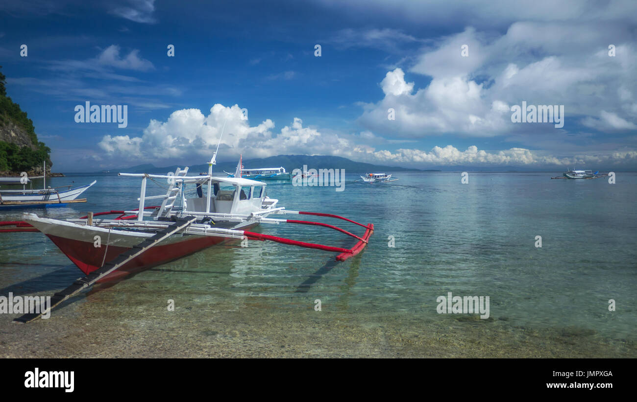 Traditionelle Filipino hölzerne Banca Auslegerboot auf Tropeninsel mit ruhigen, klaren Meer. Puerto Galera, Mindoro, Philippinen. Stockfoto