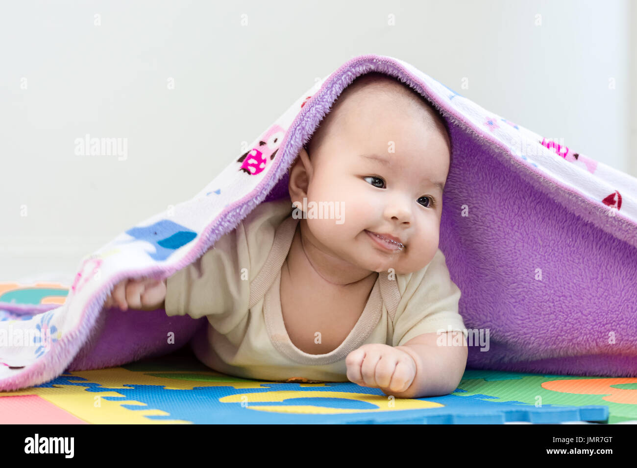 Porträt eines Mädchens entzückende Baby Baby mit Decke und Speichel liegend auf dem Bauch auf bunte Eva-Schaum Stockfoto