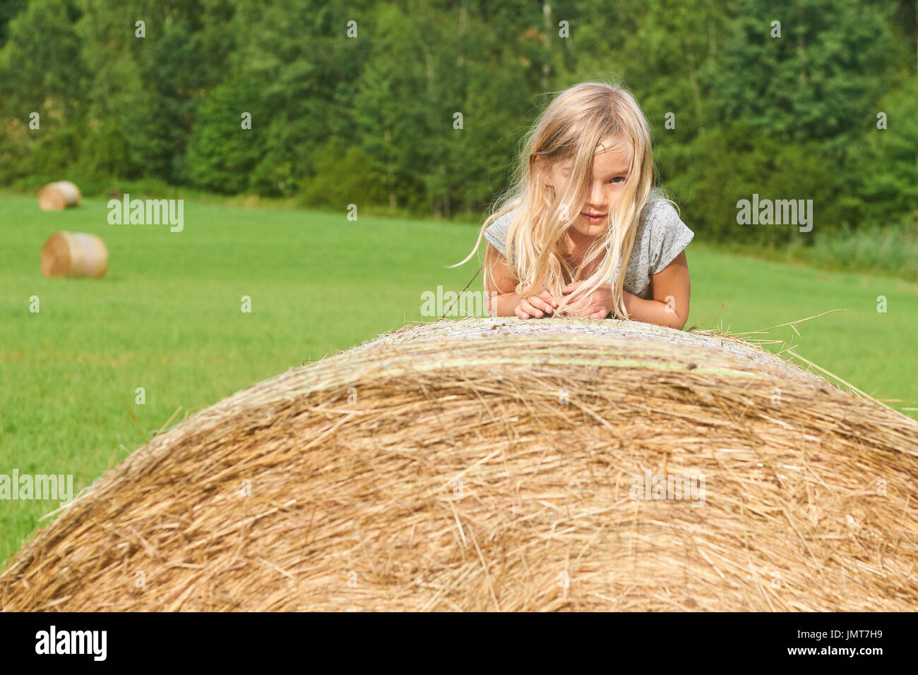 Kind blondes Mädchen von Stroh Heu Ballen in das Feld ein. Kinder Aktivitäten im Sommer Stockfoto