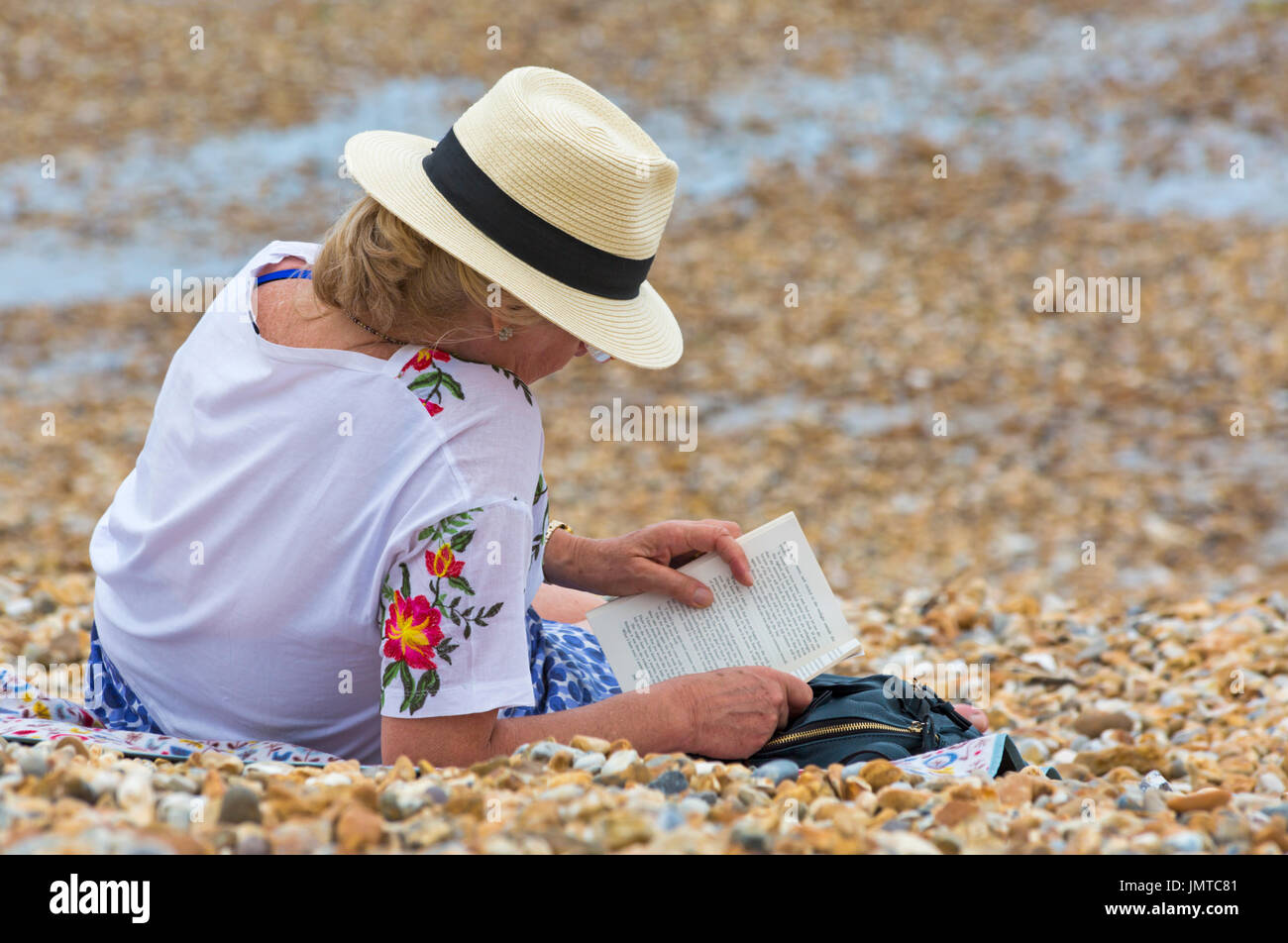 Frau liest ein Buch am Strand von Lyme Regis, Dorset im Juli Stockfoto