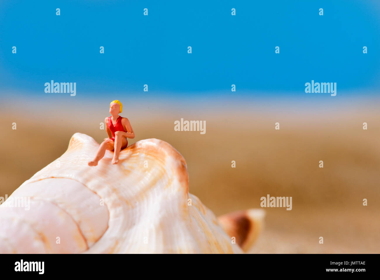 Nahaufnahme einer Miniatur-Frau mit Badeanzug entspannt auf einer Muschel am Strand, mit einem negativen Raum an der Spitze Stockfoto