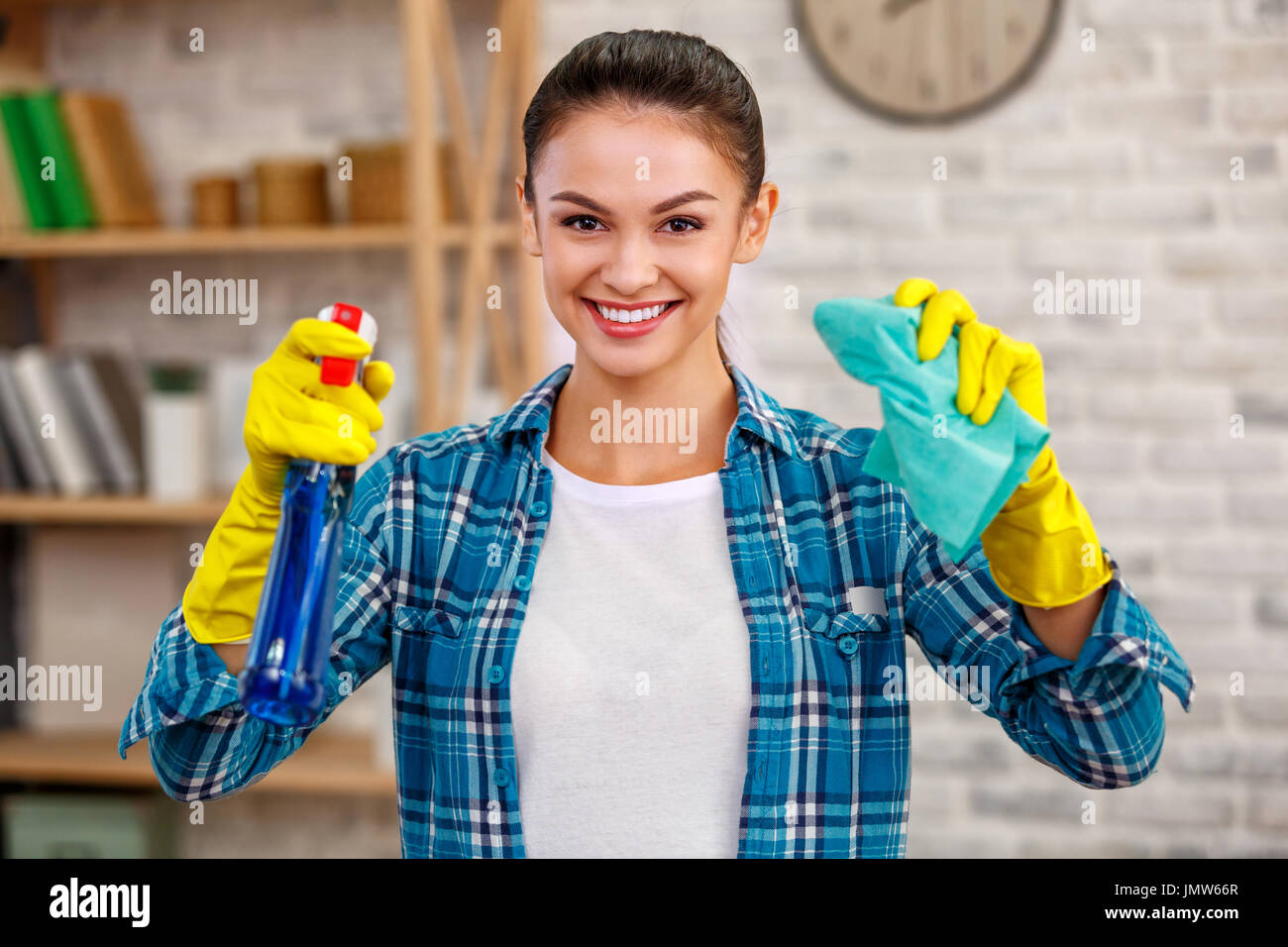 Studioaufnahme der Haushälterin. Schöne Frau Reinigungsraum. Frau mit Handschuhen, lächelnd und halten Sie die Flasche mit Desinfektionsmittel Stockfoto
