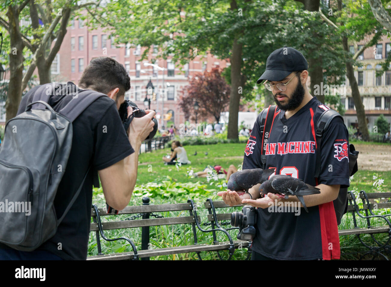Ein Tourist im Washington Square Park ernährt Tauben aus seiner Hand, während ein Freund es mit einem Foto erinnert an. New York City. Stockfoto