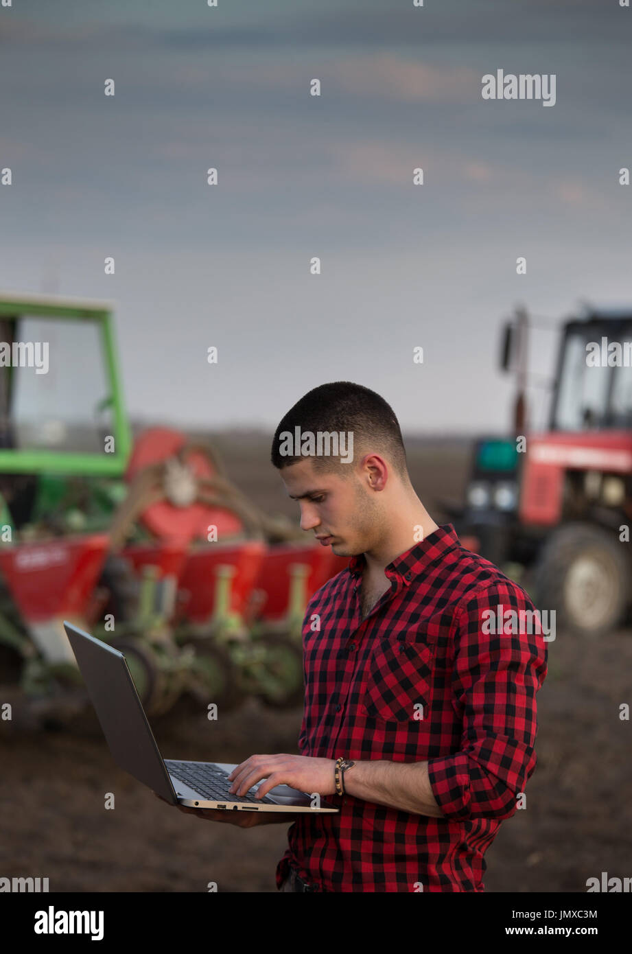 Junglandwirt mit Laptop im Feld vor Traktor mit Aussaat Ausrüstung stehen. Smart-Technologie in der Landwirtschaft Stockfoto