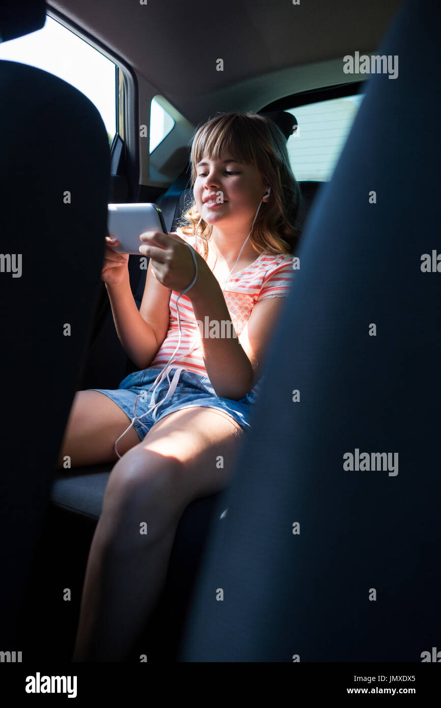 Glücklich Teenager-Mädchen in Kopfhörer mit Handy auf dem Rücksitz des Autos  Stockfotografie - Alamy