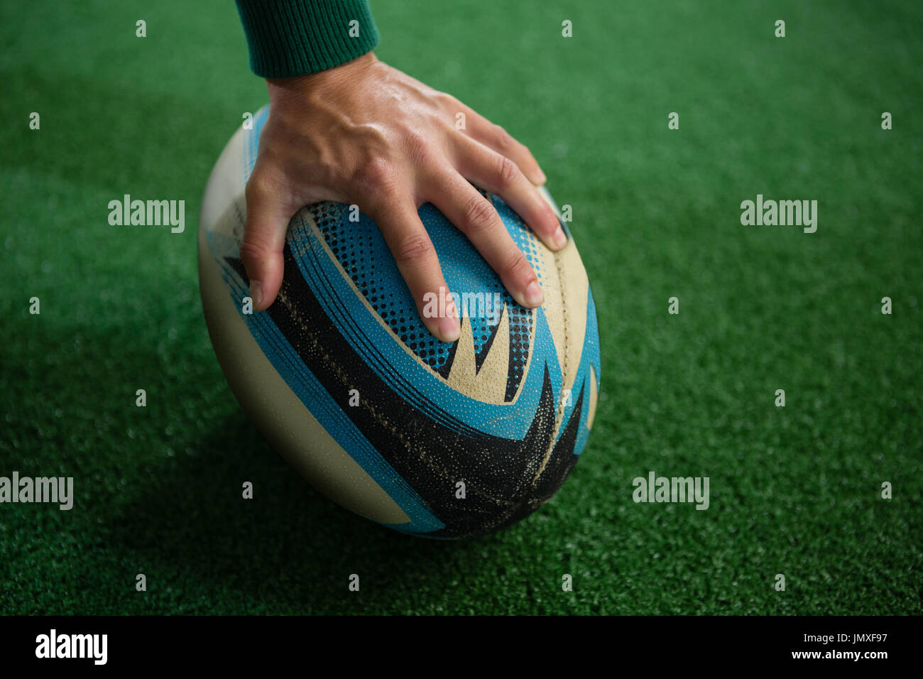 Hand der Person mit Rugby-Ball auf Feld abgeschnitten Stockfoto